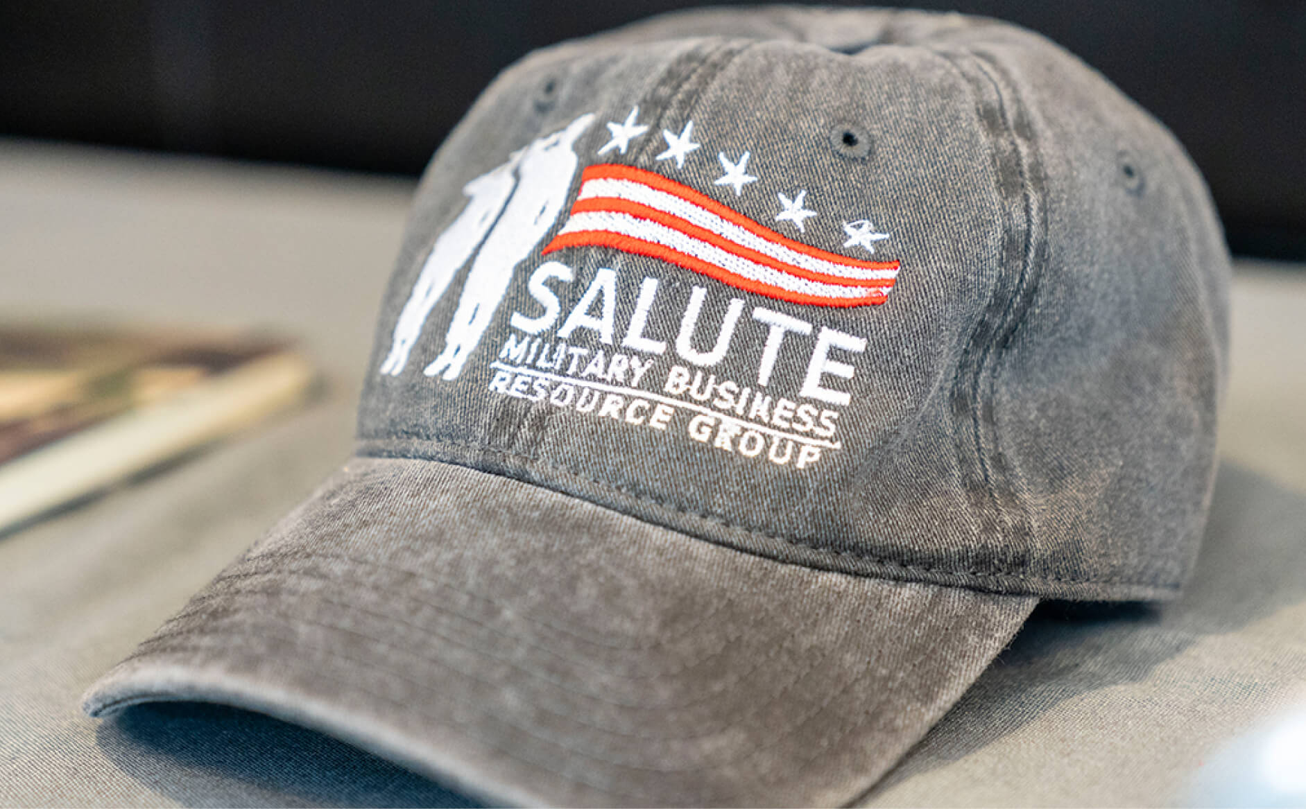 Gray ballcap with logo of white silhouette of two soldiers standing at attention, with flag logo and wording that says 